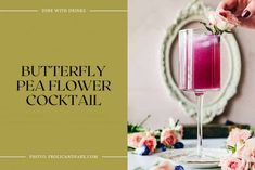 the butterfly pea - flower cocktail is served in a tall wine glass with pink flowers