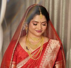 a woman in a red sari and gold jewelry looks down at her necklaces