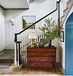 a wooden dresser sitting under a stair case next to a lamp and painting on the wall