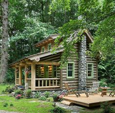 a small log cabin in the woods surrounded by greenery and flowers, with a deck leading to it