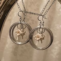 two silver circular earrings with flowers on them hanging from a metal chain in front of a mirror