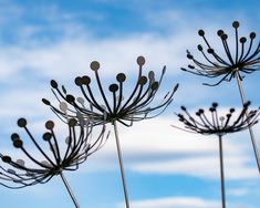 three metal flowers against a blue sky with clouds in the backgrounnds