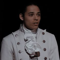 a woman wearing a white jacket and tie in front of a black background with buttons on it