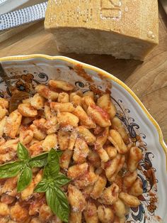 a pasta dish with basil leaves on top and bread in the backgroung