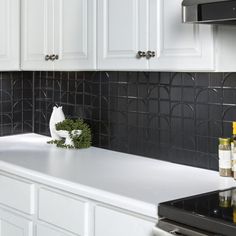 a kitchen with white cabinets and black tile backsplash, including an oven hood