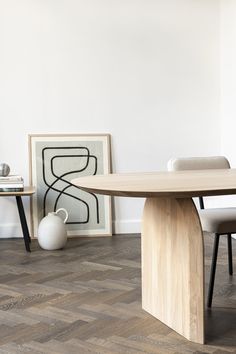 a table and chairs in a room with white walls, wood flooring and artwork on the wall