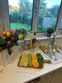 a kitchen counter topped with lots of fruit and vegetables next to a window filled with flowers