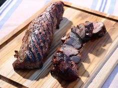 two pieces of meat sitting on top of a wooden cutting board