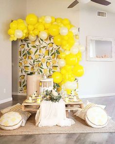 a table topped with lots of yellow and white balloons next to a wall covered in lemons