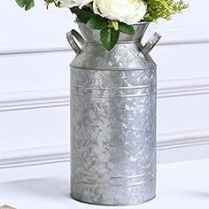 a metal vase with white flowers in it on a table next to a planter