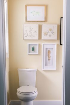 a white toilet sitting in a bathroom next to framed pictures on the wall above it