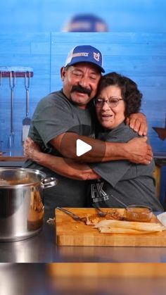 a man and woman hugging in front of a pot full of food on a table