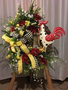 a rooster wreath with red, yellow and white flowers in it sitting on a easel