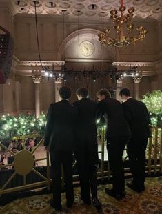 three men in suits stand at the top of a balcony looking out onto an indoor christmas tree