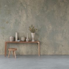 a wooden table topped with vases and flowers next to a wall covered in cement