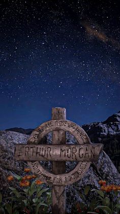 a wooden sign sitting on the side of a mountain under a sky filled with stars