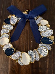 a blue and white wreath with gold trim on a wooden table next to a blue ribbon