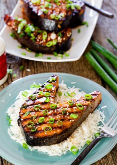 two pieces of grilled salmon on top of white rice with green onions and scallions