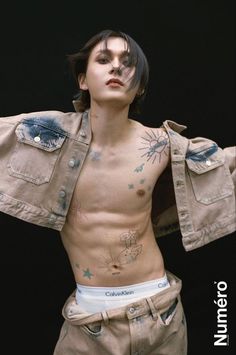 a male model with tattoos on his chest and shirtless torso is posed in front of a black background