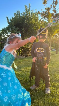 two young children dressed up as batman and princesses in the grass, one holding a wand