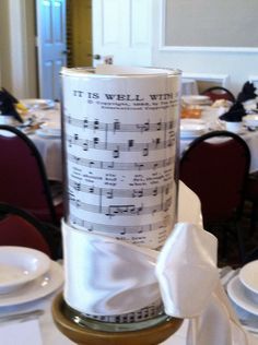 a can with sheet music on it sitting on top of a white tablecloth covered table