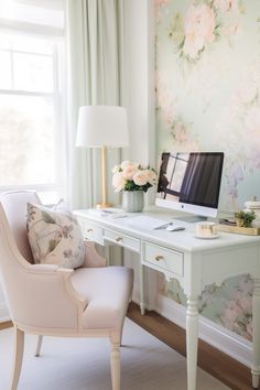 a desk with a computer on top of it next to a flowered wallpaper