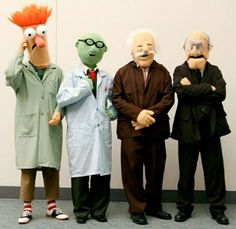 five puppets are posed in front of a white wall and one is wearing a lab coat