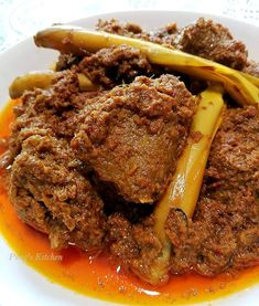 a white plate topped with meat and vegetables covered in gravy on top of a table