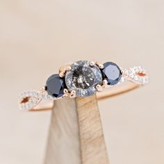 an engagement ring with three different colored stones on it's side, sitting on top of a piece of wood