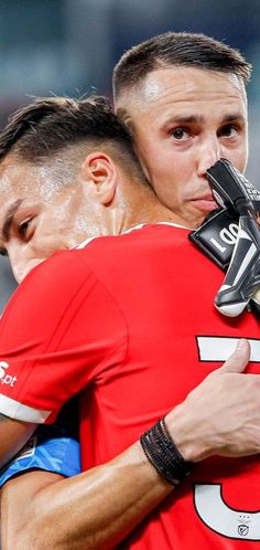 two soccer players hugging each other in the middle of a game, with one player wearing a glove