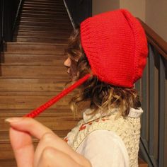 a woman wearing a red knitted hat while holding a toothbrush in her hand