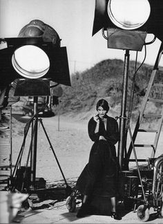 a black and white photo of a woman sitting in front of some lighting equipment on the ground