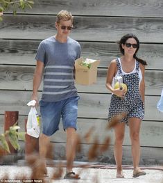 a man and woman walking down the street with boxes in their hands, carrying groceries