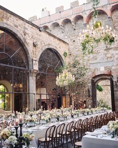 the tables are set up in front of an old stone building with arched windows and chandeliers