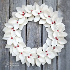 a wreath made out of white flowers on top of a wooden fence with red berries