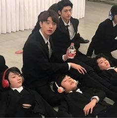 group of young men in suits and headphones sitting on the floor with one holding a bottle