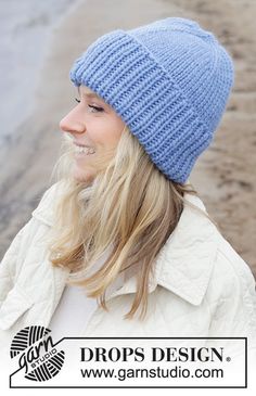 a woman wearing a blue knitted beanie hat looking off into the distance with her hair blowing in the wind