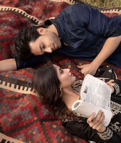 a man and woman laying on top of a colorful blanket reading a book next to each other