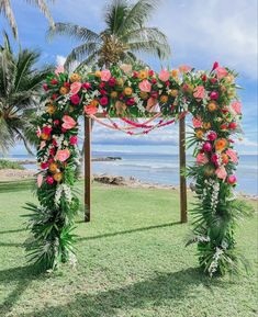 an outdoor wedding setup with flowers and greenery on the grass by the ocean in front of palm trees