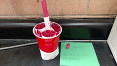 a red cup filled with liquid next to a green piece of paper