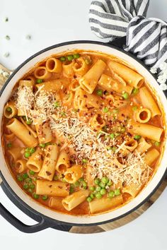 a pot filled with pasta and peas on top of a wooden cutting board next to a striped napkin