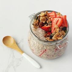 a glass jar filled with granola and strawberries next to a wooden spoon on a white surface