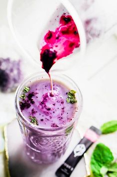 a cup filled with blueberry smoothie on top of a white table next to green leaves