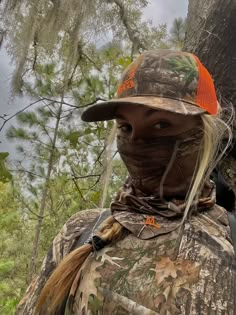 a woman wearing a hunting hat and camouflage clothing stands in front of a large tree