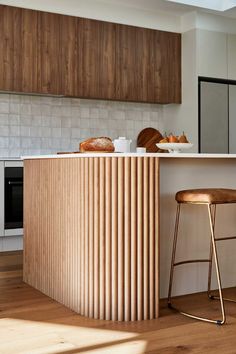 a kitchen with wooden cabinets and stools in front of an island counter that has bread on it