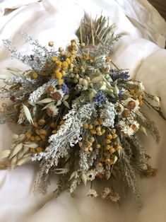 a bunch of dried flowers laying on top of a white cloth covered bedding area