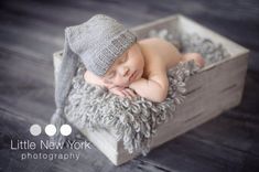 a baby is sleeping in a crate with a gray hat on it's head