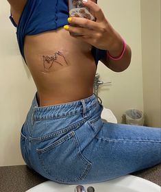 a woman is sitting on the bathroom sink taking a selfie with her cell phone