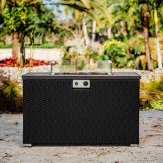 a large black box sitting on top of a cement ground next to trees and bushes