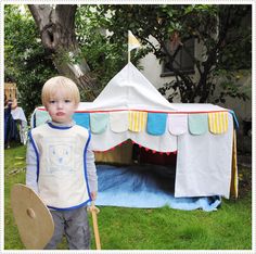 a little boy standing in front of a tent with a paddle and shield on it